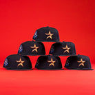 Six 6am in Texas Navy Red White New Era Hat 5950 Fitted caps, designed by Axel Reynoso with colorful side patches, are arranged in a pyramid formation against a bright red background. Each features the signature orange and white star logo on the front.