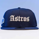 The Fat Elvis OE ASG Dark Blue New Era Hat 5950 Fitted features “Astros” embroidered in white gothic letters on the front, shown from the front against a light blue background.