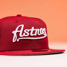 The Big Puma Cardinal White Script New Era Hat 5950 Fitted features a vibrant red design with "Astros" in cardinal white script on the front, inspired by Big Puma and set against a light orange background.