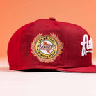 The Big Puma Cardinal White Script New Era Hat 5950 Fitted by New Era, in red with commemorative “1965-2006 Celebrating 45 Years” side patch, is displayed on an orange background.