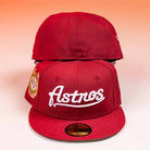 Two The Big Puma Cardinal White Script New Era Hat 5950 Fitted caps sit on a white surface with an orange gradient background. The front cap displays “Astros” in Cardinal White Script and a round side patch; only the back of the other is visible.