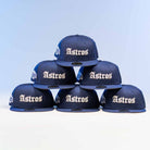Six Fat Elvis OE ASG Dark Blue New Era Hat 5950 Fitted caps are arranged in a pyramid shape, with "Astros" on the front, set against a light blue background.