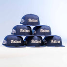 Six Fat Elvis OE ASG Dark Blue New Era Hat 5950 Fitted caps are stacked in a pyramid, each displaying a white embroidered Astros logo on the front and a side patch, set against a light blue and white background.