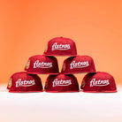 Six The Big Puma Cardinal White Script New Era Hat 5950 Fitted caps are arranged in a pyramid against an orange background. Each features “Astros” script on the front and a patch on the left side.