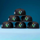 Six black Flamingo and Chill Bo Bundy 2022 Houston Astros New Era Hat 5950 Fitted caps are stacked in a pyramid. Each features a vibrant, cartoon-style embroidered patch on the front, set against a blue gradient background.