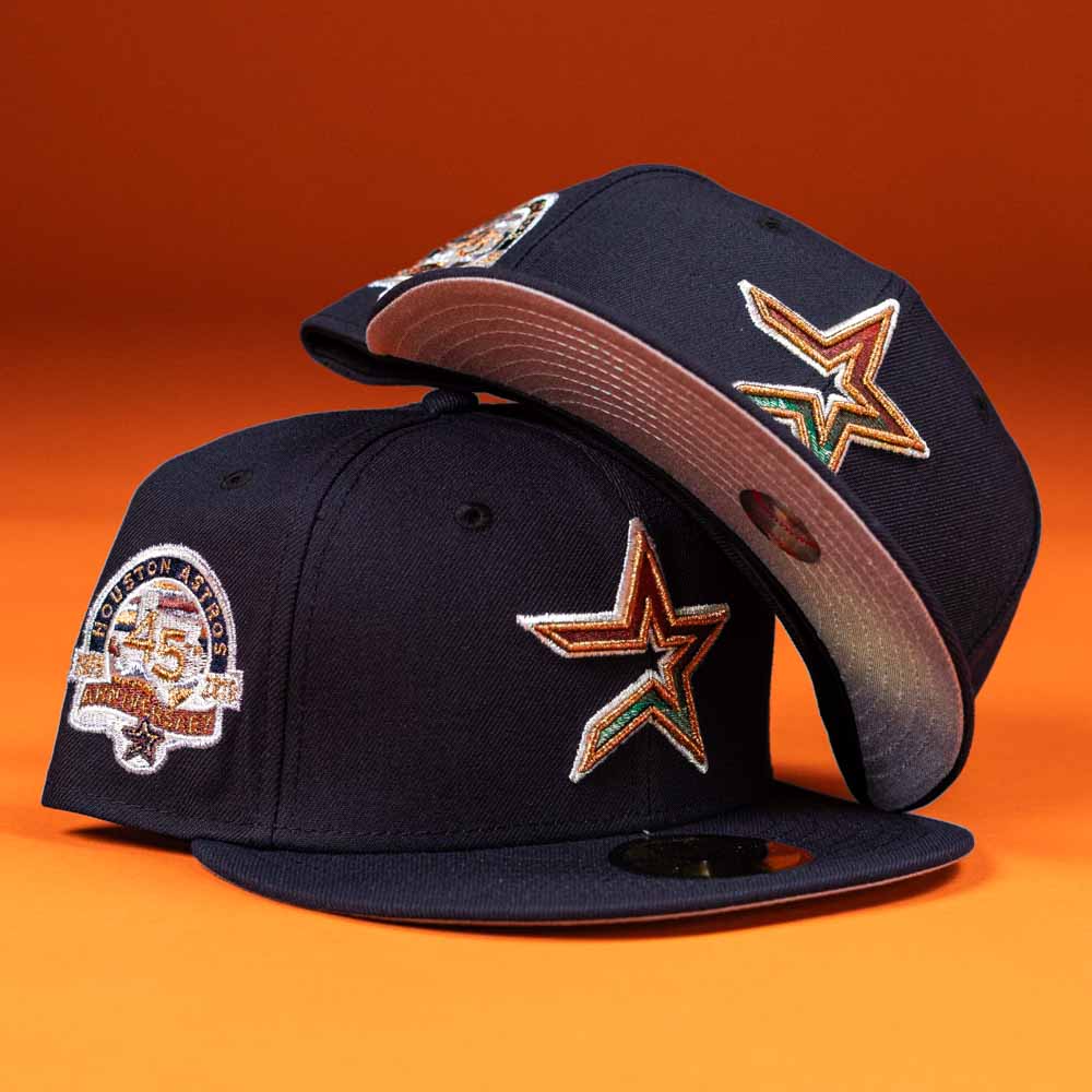 Two Highclass 45th Houston Astros New Era Hat 5950 Fitted caps in navy blue sit on an orange background, displaying star logos front and a 45th anniversary patch side, plus pink underbrims with decorative stitching.