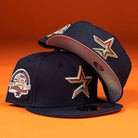 Two Highclass 45th Houston Astros New Era Hat 5950 Fitted caps in navy blue sit on an orange background, displaying star logos front and a 45th anniversary patch side, plus pink underbrims with decorative stitching.