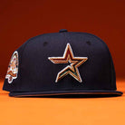 The Highclass 45th Houston Astros New Era Hat 5950 Fitted is a navy blue fitted cap featuring an embroidered gold, orange, and white Astros star logo on the front and a colorful side patch, shown against an orange background.
