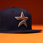 The Highclass 45th Houston Astros New Era Hat 5950 Fitted is a black cap with a stitched multicolored star logo on the front, inspired by the Astros, displayed against an orange background.