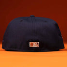 The Highclass 45th Houston Astros New Era Hat 5950 Fitted is displayed from the back, showcasing the MLB logo in white and orange stitching on navy blue, set against an orange background.