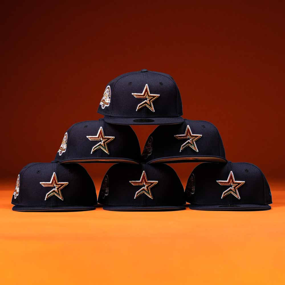 Six Highclass 45th Houston Astros New Era Hat 5950 Fitted hats with gold star logos are stacked in a pyramid against an orange background, showcasing their iconic style.