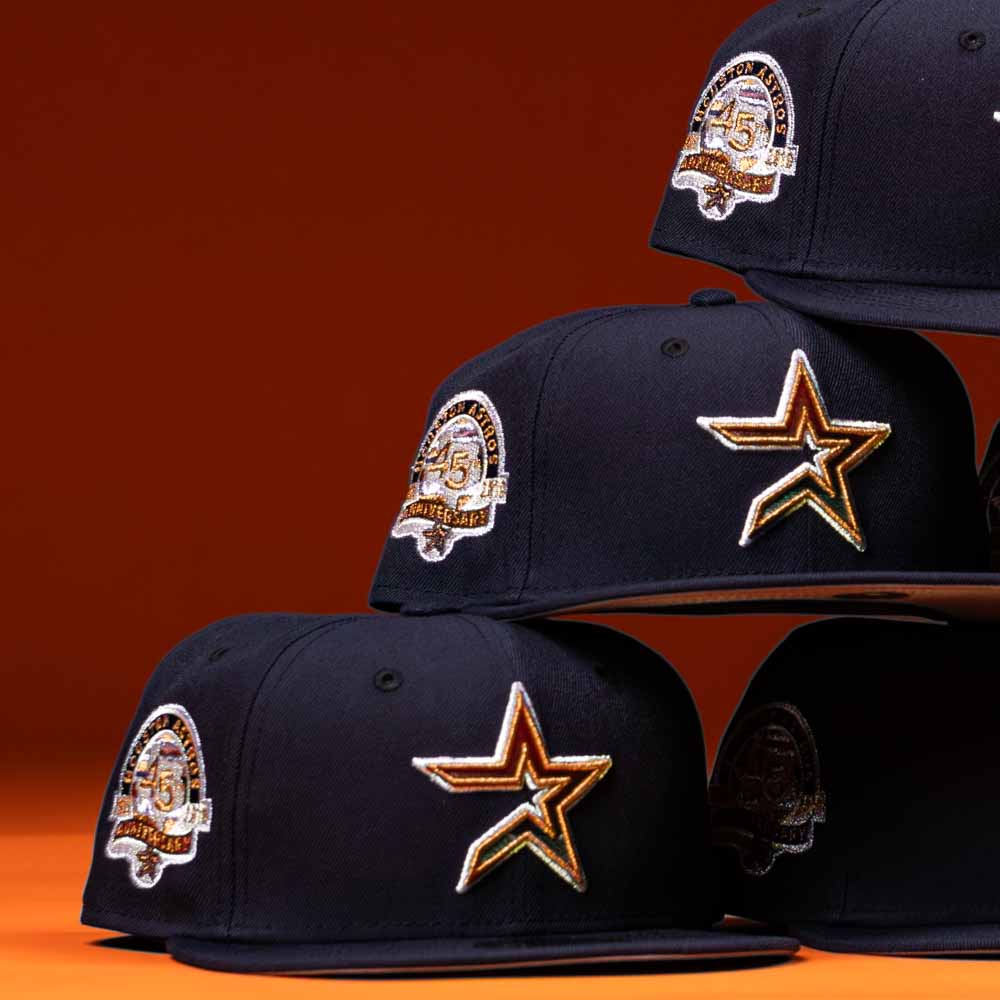Five Highclass 45th Houston Astros New Era Hat 5950 Fitted caps are stacked in two rows, each black with a gold and white Astros star front logo and “45th anniversary” patch on the side, set against an orange background.