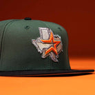 The El Jager Mountain Orange New Era Hat 5950 Fitted features a green crown, black brim, and an embroidered orange and silver star over a Texas state outline, shown on an orange background.