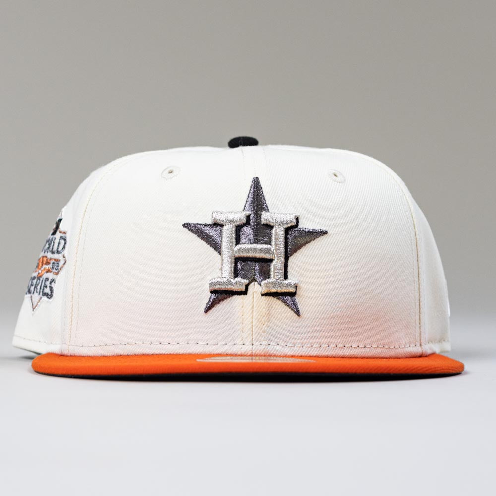 The Orange Soda New Era WS22 Houston Astros 5950 Fitted Hat features a white crown, orange brim, black star, and silver H logo on the front, with a partial World Series patch on the side for added team pride and style.