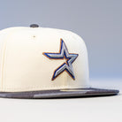 The Dark:30 New Era Chrome Black Camo Houston Astros 5950 Fitted Hat features a cream crown, black brim, and an embroidered blue and silver star with a gold outline on the front, all set against a plain, neutral background.