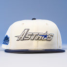 The International Flea Bo Bundy New Era Houston Astros 5950 Fitted Hat features a white and navy design, Astros metallic embroidery on the front, a commemorative patch on the left, and a light blue-to-white gradient background.