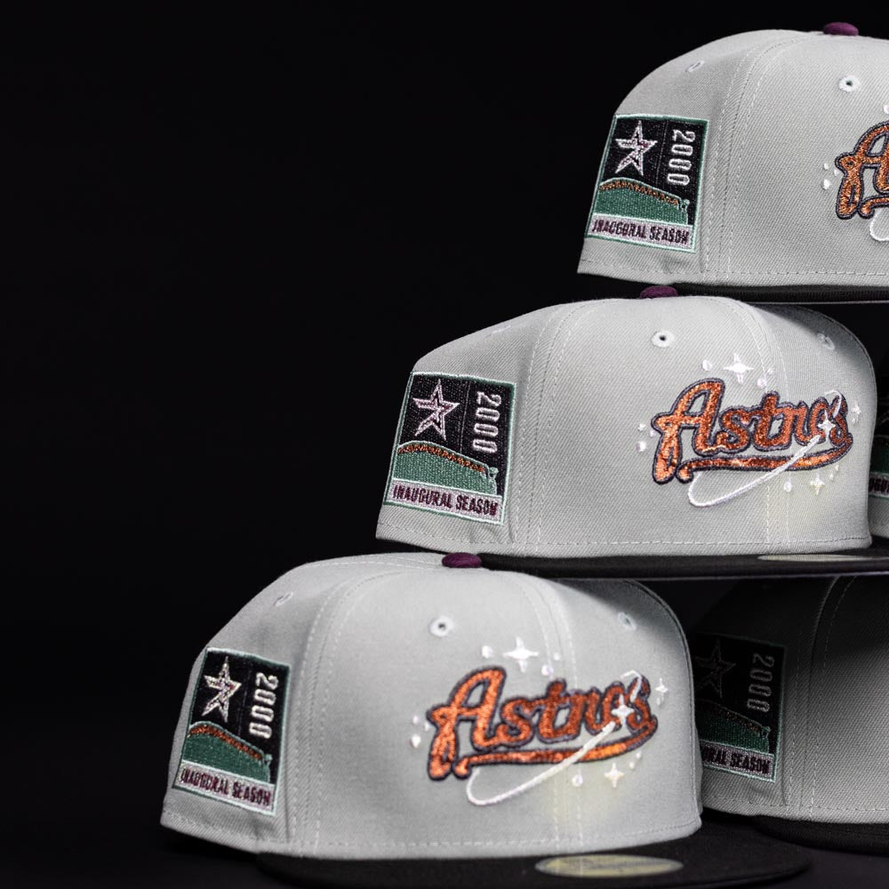 A stack of Pixie Dust New 2000 Houston Astros New Era Hat 5950 Fitted hats is displayed against a black background, featuring the team logo on the front and a "2000 Inaugural Season" patch on the side.