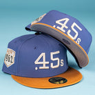 Two Harbor Mark Canvas Houston Astros New Era Hat 5950 Fitted caps in blue with gold brims, “.45s” in large white letters on the front and a “HOUSTON 1962” side patch, displayed on a light blue background.