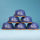 Six Harbor Mark Canvas Houston Astros New Era 5950 Fitted hats with blue crowns and orange brims are stacked in a pyramid against a blue background, each featuring "45s" in white on the front.