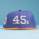 The Harbor Mark Canvas Houston Astros New Era 5950 Fitted Hat features a blue crown, brown brim, bold white .45s front embroidery, and a white patch with black text on the left honoring the Astros. Background is solid light blue.