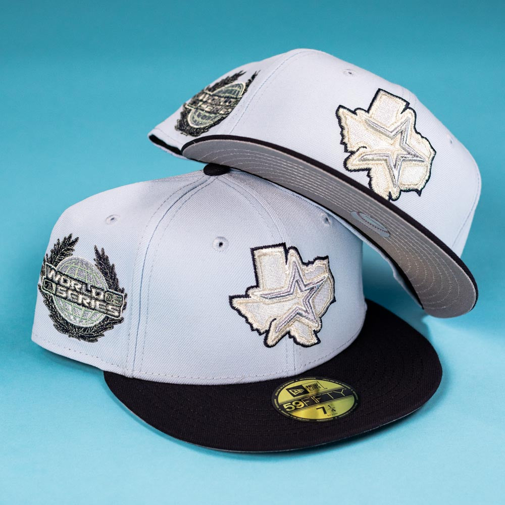 Two light gray Hard Freeze WS05 Houston Astros New Era 5950 fitted hats with black brims, Texas state and star patches on the front, World Series logos on the side, displayed on a blue background.