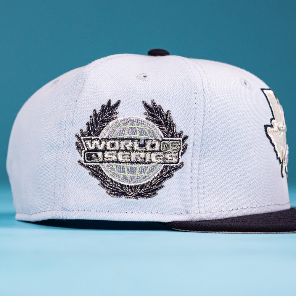 The Hard Freeze WS05 Houston Astros New Era 5950 Fitted hat features a light color and a World Series patch with globe and laurel design on the side, shown on a blue surface and background.