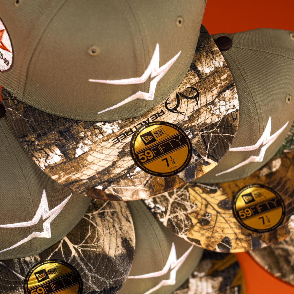 A stack of Pre-Order Wall Hanger New Era Bark Real Tree Houston Astros 5950 Fitted hats with camo brims, white embroidered logos, and gold "59FIFTY 7 1/2" stickers—available for pre-order or in-store pick-up.