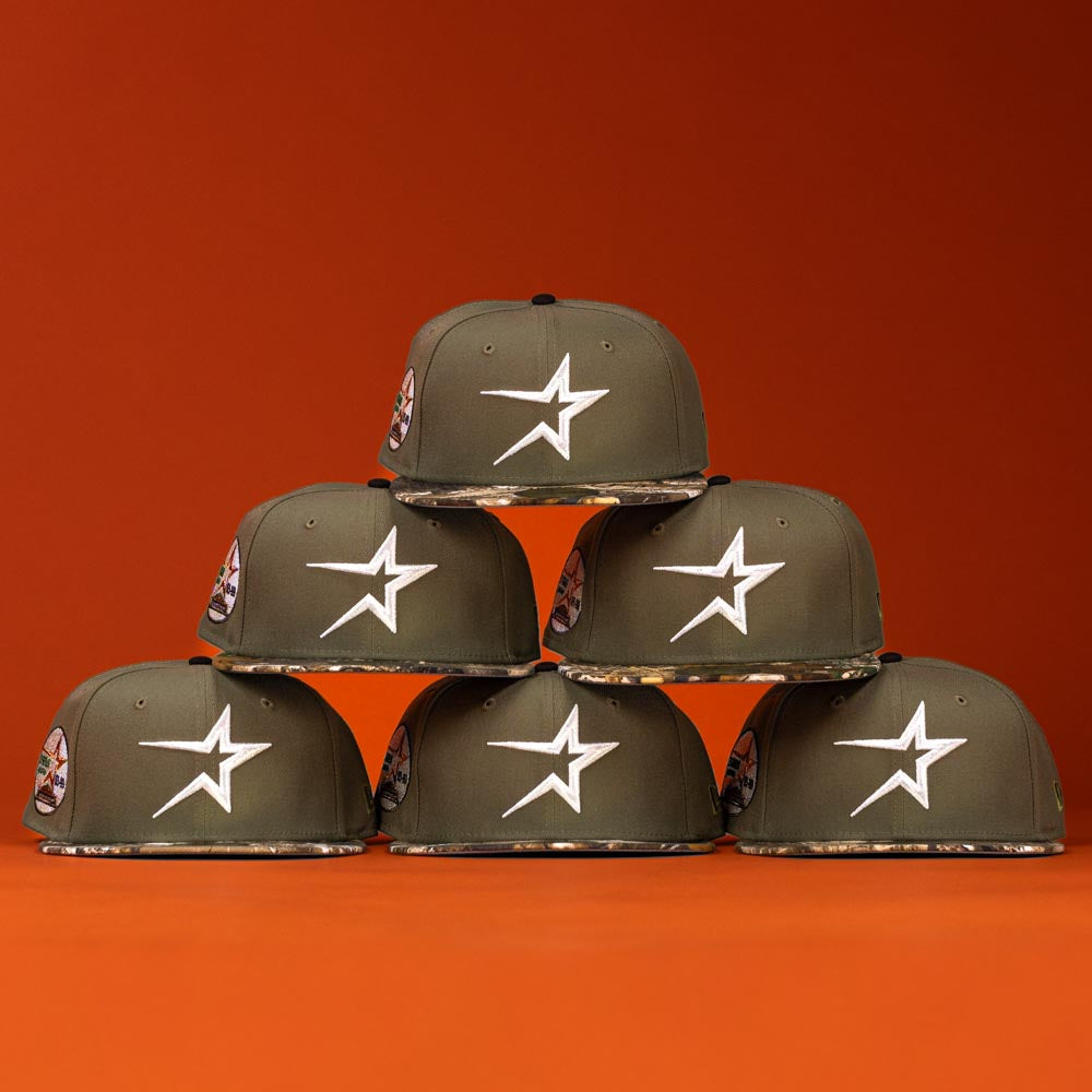 Six Pre-Order Wall Hanger New Era Bark Real Tree Houston Astros 5950 Fitted hats are stacked in a pyramid, showing patterned brims and side patches, against an orange background. Available for pre-order with flexible shipping options.