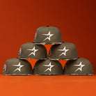 Six Pre-Order Wall Hanger New Era Bark Real Tree Houston Astros 5950 Fitted hats are stacked in a pyramid, showing patterned brims and side patches, against an orange background. Available for pre-order with flexible shipping options.