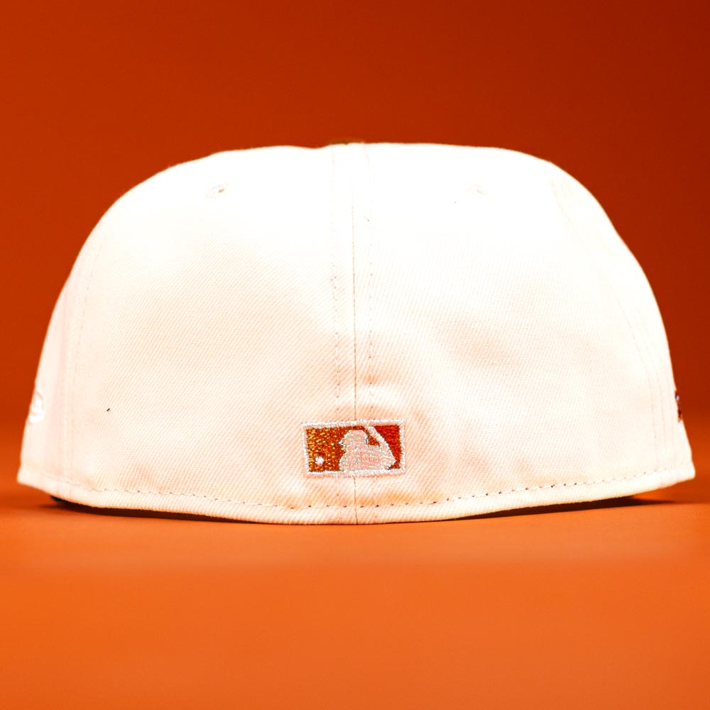 The Rustic Sunset Houston Astros New Era Hat 5950 Fitted is shown upside down, highlighting the small MLB logo on the back, displayed against an orange background.