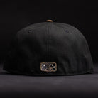 The Midnight Cowboy Sugarland Space Cowboys New Era 5950 Fitted Hat is shown from the back, featuring a small gold and black star and figure patch near the bottom—subtly referencing the Space Cowboys. The hat and background are both black.