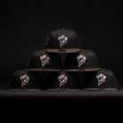 A pyramid stack of six Midnight Cowboy Sugarland Space Cowboys New Era 5950 Fitted hats—black with tan brims and featuring the embroidered Space Cowboys logo—stands out against a dark background.