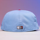 The Sicko Mode Rushmore 2017 B Blue Black Houston Astros New Era Hat 5950 Fitted is displayed from the back, showcasing a rectangular patch with a bear and red triangle. The softly lit background glows in purple and pink hues.