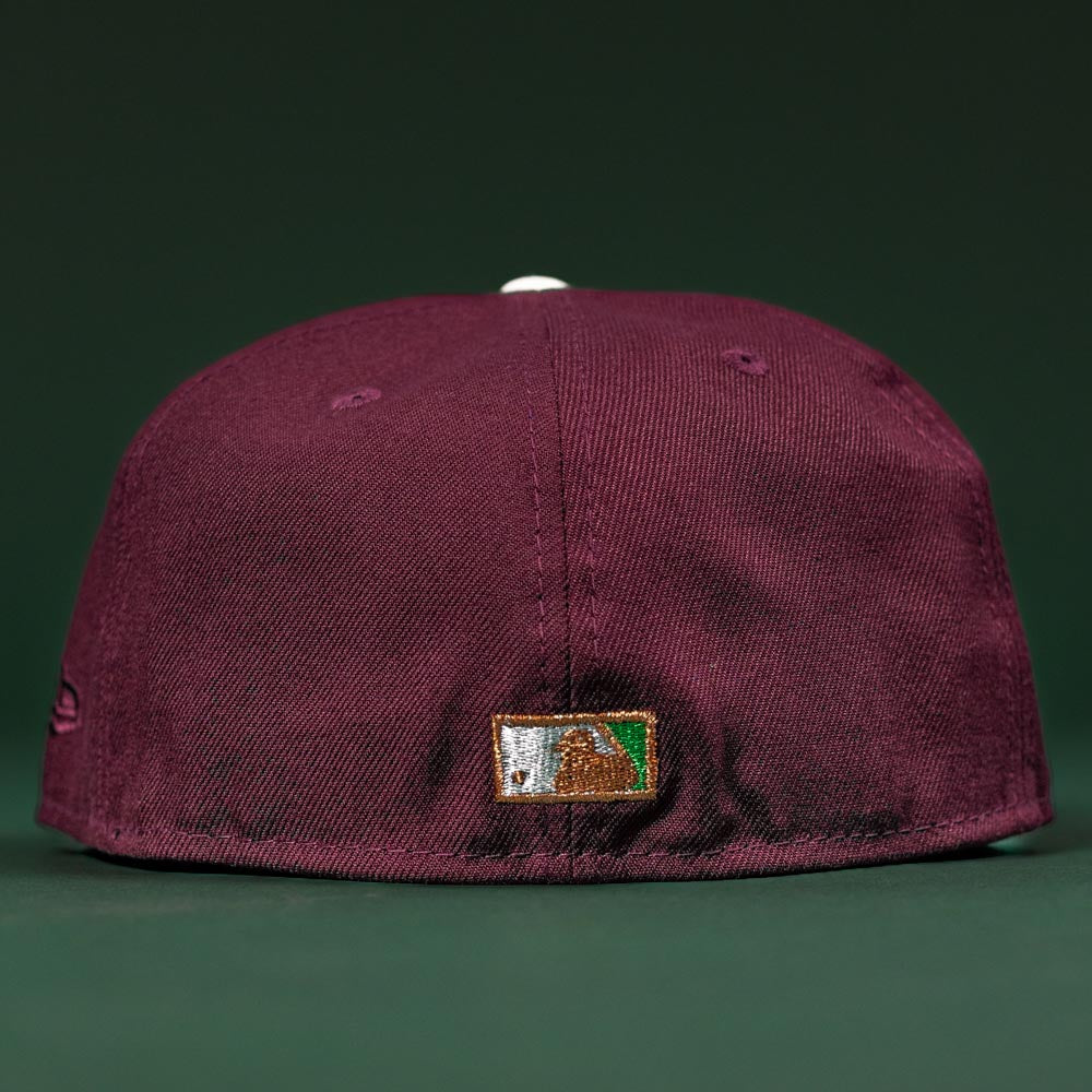 The Pinkerton 2.0 Rushmore 2000 Maroon Houston Astros New Era Hat 5950 Fitted is shown from the back, displaying a small embroidered logo patch near the bottom edge against a dark green background.