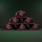 Six maroon caps, including the Pinkerton 2.0 Rushmore 2000 Maroon Houston Astros New Era Hat 5950 Fitted, are stacked in a pyramid. Each features vibrant Texas patches, embroidered details, and flag accents on a dark green background.