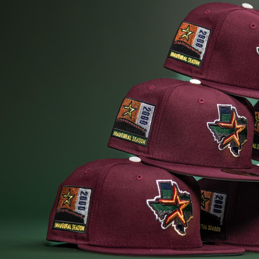 Pinkerton 2.0 Rushmore 2000 Maroon Houston Astros New Era 5950 Fitted hats with embroidered patches—state of Texas, a star, "2000," and "Inaugural Season"—are stacked on a dark green background.