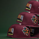Pinkerton 2.0 Rushmore 2000 Maroon Houston Astros New Era 5950 Fitted hats with embroidered patches—state of Texas, a star, "2000," and "Inaugural Season"—are stacked on a dark green background.