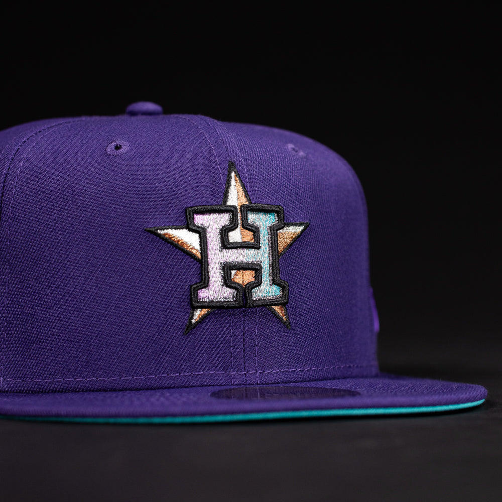 The DAY N HOU Rushmore WS05 Purple Teal Houston Astros New Era 5950 Fitted Hat features a large embroidered H with a gold star on the front, a flat brim with teal underside, and a bold black and purple design.