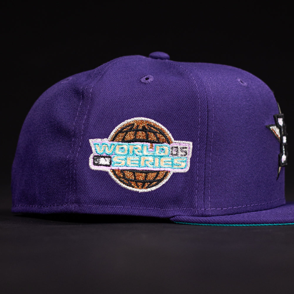 The DAY N HOU Rushmore WS05 Purple Teal Houston Astros New Era 5950 Fitted Hat features a World Series logo with a brown globe and blue accents on the side, inspired by the Astros, shown against a black background.