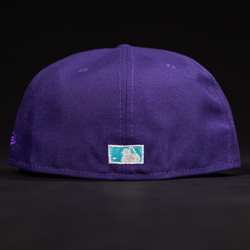 A close-up of the back of the DAY N HOU Rushmore WS05 Purple Teal Houston Astros New Era Hat 5950 Fitted shows a small rectangular MLB logo patch above the brim, set against a black background.