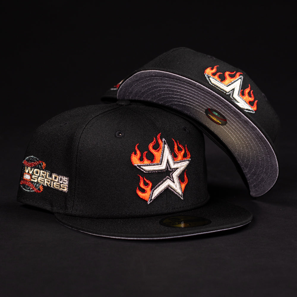The La Flame Rushmore WS05 Fire Black Houston Astros New Era 5950 Fitted cap features a flaming star logo, a World Series side patch, and a unique underbrim design, displayed against a dark background.