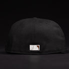 The La Flame Rushmore WS05 Fire Black Houston Astros New Era 5950 Fitted Hat is shown from the back, displaying a small rectangular patch with white and brown stitching near the bottom edge. The background is black.