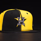 The Hazmat Rushmore Gold Black Pinwheel Houston Astros New Era 5950 Fitted Hat features a split black and yellow design with a large embroidered H and star logo on the front.