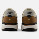 Rear view of two 933 ONE Quicksand Sea Salt Gray Andrew Reynolds New Balance Numeric Suede Skateboarding Shoes, featuring beige, brown, and black details with the NB logo on each heel and a heritage design inspired by classic Andrew Reynolds skate shoes, set against a plain white background.