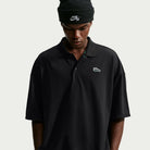 Person wearing an AF1 Black Court Green Solid Break Polo IV0597010 Polo Top Nike SB Skateboarding with a small graphic logo on the chest and a black beanie.