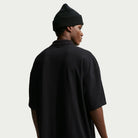 A person viewed from behind, wearing a black AF1 Black Court Green Solid Break Polo IV0597010 Polo Top Nike SB Skateboarding and a black beanie.