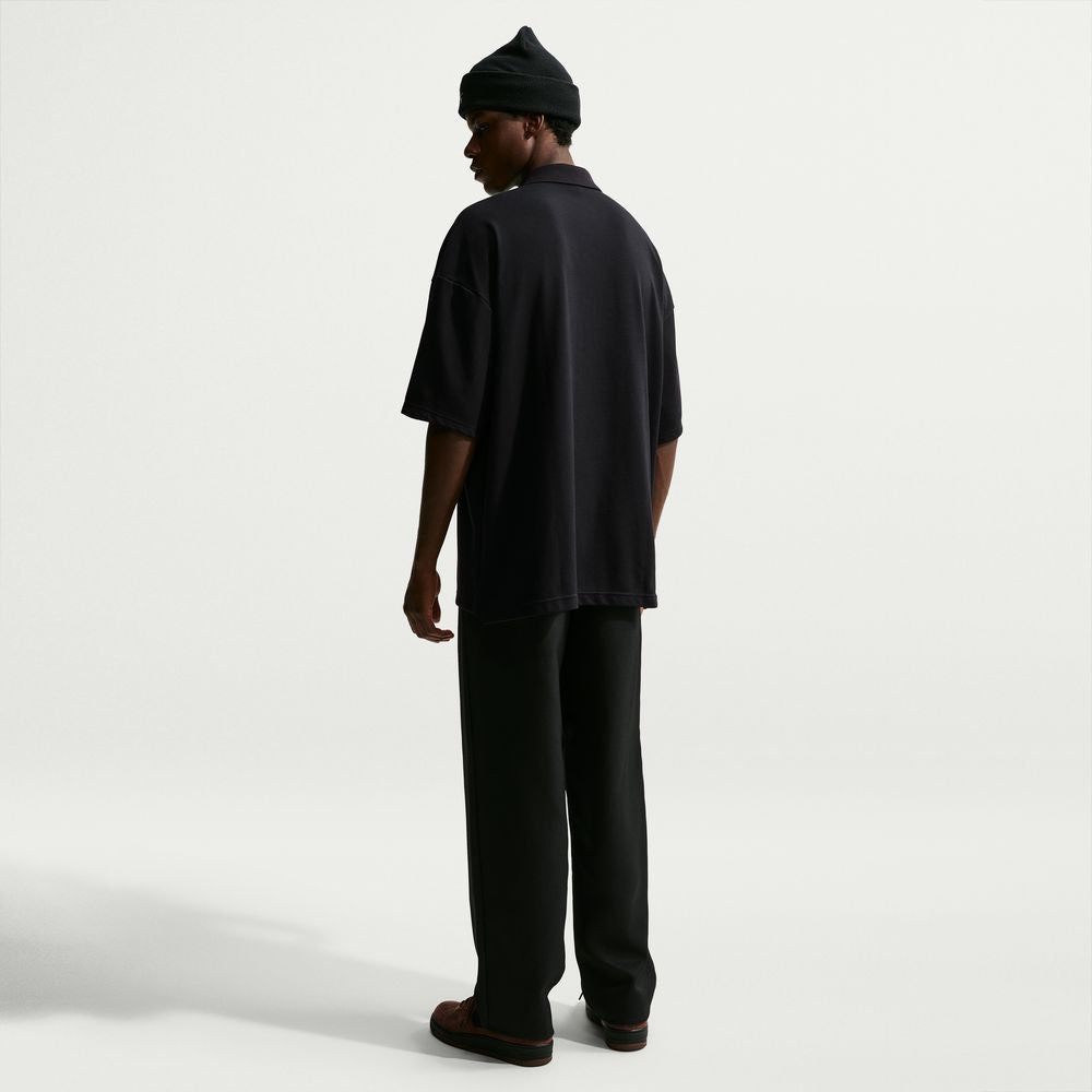 A person from behind wearing a black beanie, black trousers, and an AF1 Black Court Green Solid Break Polo IV0597010 Polo Top Nike SB Skateboarding.