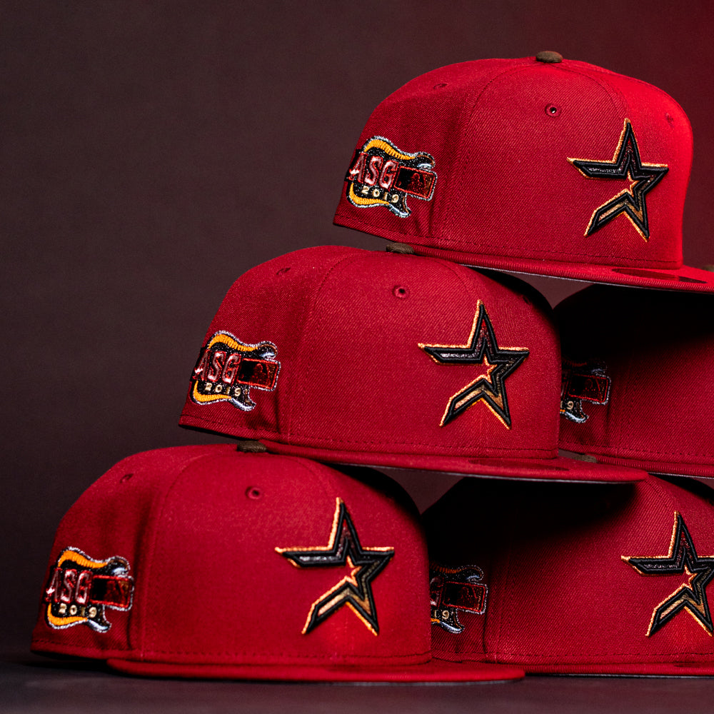 A stack of ASG19 Bred Houston Astros New Era Hat 5950 Fitted caps with a gold-outlined star on the front and an SG 2015 side patch, displayed against a dark background.