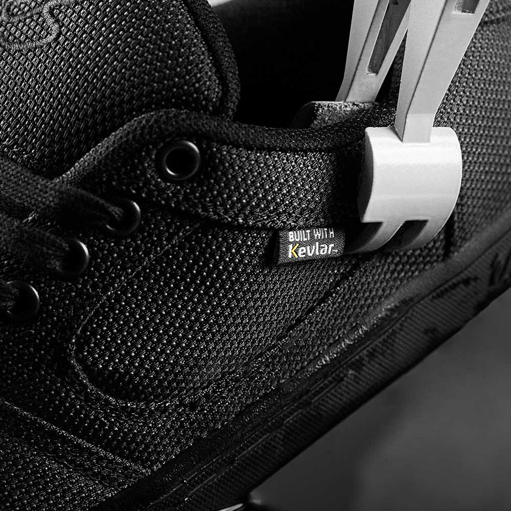 Close-up of the Accel Kevlar Black Es skateboarding shoe featuring a woven texture, a tag reading BUILT WITH Kevlar, and a white security tag—emphasizing its enhanced durability for skateboarders.