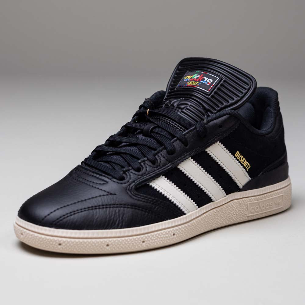The Busenitz Black White HQ4708 Adidas Skateboarding Suede Shoes feature a black upper with white stripes, a beige sole, gold "Busenitz" text on the side, and a colorful adidas logo on the tongue. Displayed on a plain gray background.